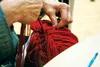 Midge Johnson ties red yarn to a pre-crocheted beanie to make a 'princess' wig, inspired by Disney's 'Ariel,' for a young girl with hair loss due to cancer on Saturday, Oct. 17, for the first