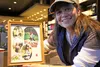 Tami Bara smiles for a photo in an Eagle River Starbucks on Friday afternoon with a framed collage of photos showing her ability to 'outfish' her husband Jeff. A fundraiser is being held for 