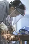 A shower of sparks shoots off the wheel of a grinder C.J.
Weatherford of Wasilla uses to finish the surface of a metal cutout
of the state of Alaska. Weatherford was among 18 foster youth
par