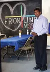 The Rev. Minoj Ingle stands in front of the Frontline Mission logo decorating one wall of the soup kitchen. Staff at the mission staged an open house for local and state officials June 17. BR