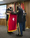 Brig. Gen. Douglas Lowrey, left, and Command Sgt. Maj. Sean Rice, right, unfurl the one-star flag during Lowrey's promotion ceremony at the U.S. Army Security Assistance Command headquarters,