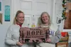 Family Promise Mat-Su Executive Director, Ginger Bear [right] and Case Manager/Program Coordinator, Nancy Retallick [left] show a custom sign made for the upcoming H.O.P.E. Navigation Center.