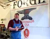 Forge 33 owner Kevin Adams proudly displays one of his most recent pieces, a San-mai bowie style blade with a stacked cork handle, including a woolly mammoth tusk for the center spacer and a 