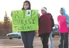 Kazi Warner and Donna Ratcliffe-Woosley, wearing a red jacket, hold up signs along the Parks Highway in front of Wasilla Lake Wednesday urging drivers to honk in support, to ask questions and
