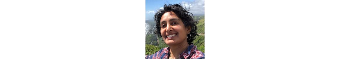 A photo of me, an Indian American woman in my early 40s, with short wavy black hair, smiling in front of distant green hills and blue sky.