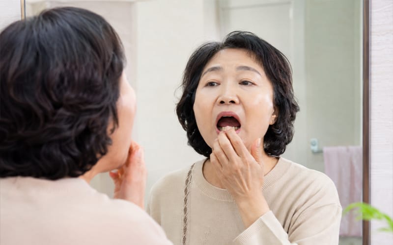 An elderly patient looking at their teeth in front of a mirror with their mouth open.