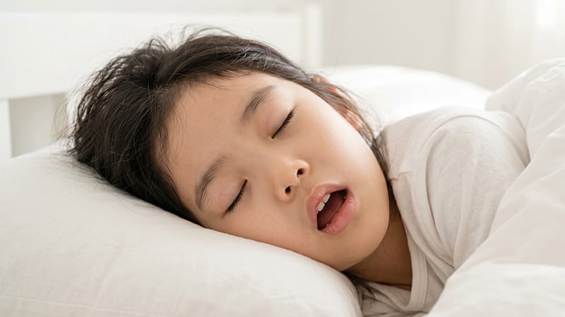 A young child sleeping on a bed with their mouth open
