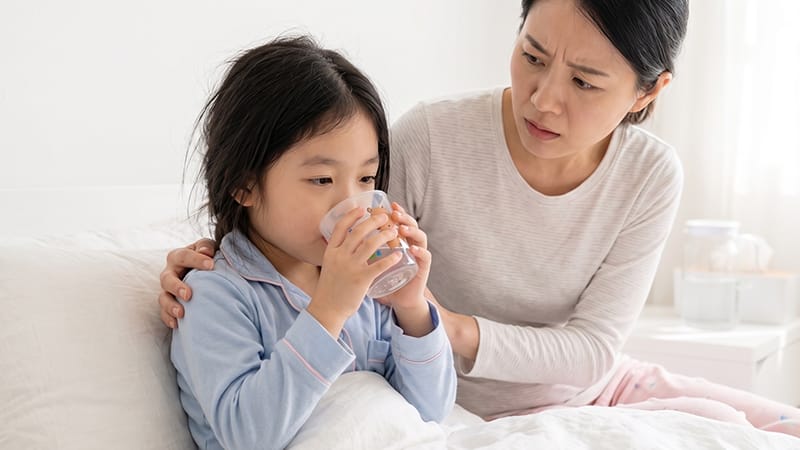 A young child drinking water while a worried parent watches alongside
