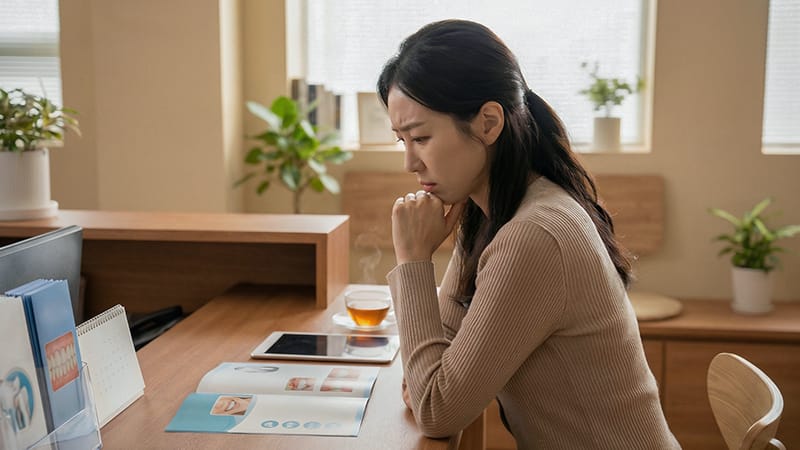 진료실 데스크에서 태블릿이나 팸플릿을 보며 깊은 고민에 잠긴 2030 여성 환자의 모습