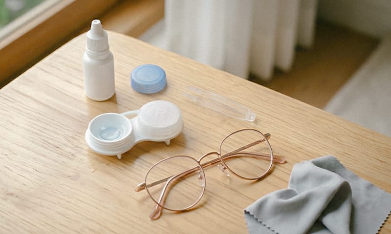 안약통, 렌즈통과 콘택트 렌즈, 집게, 안경이 놓인 모습