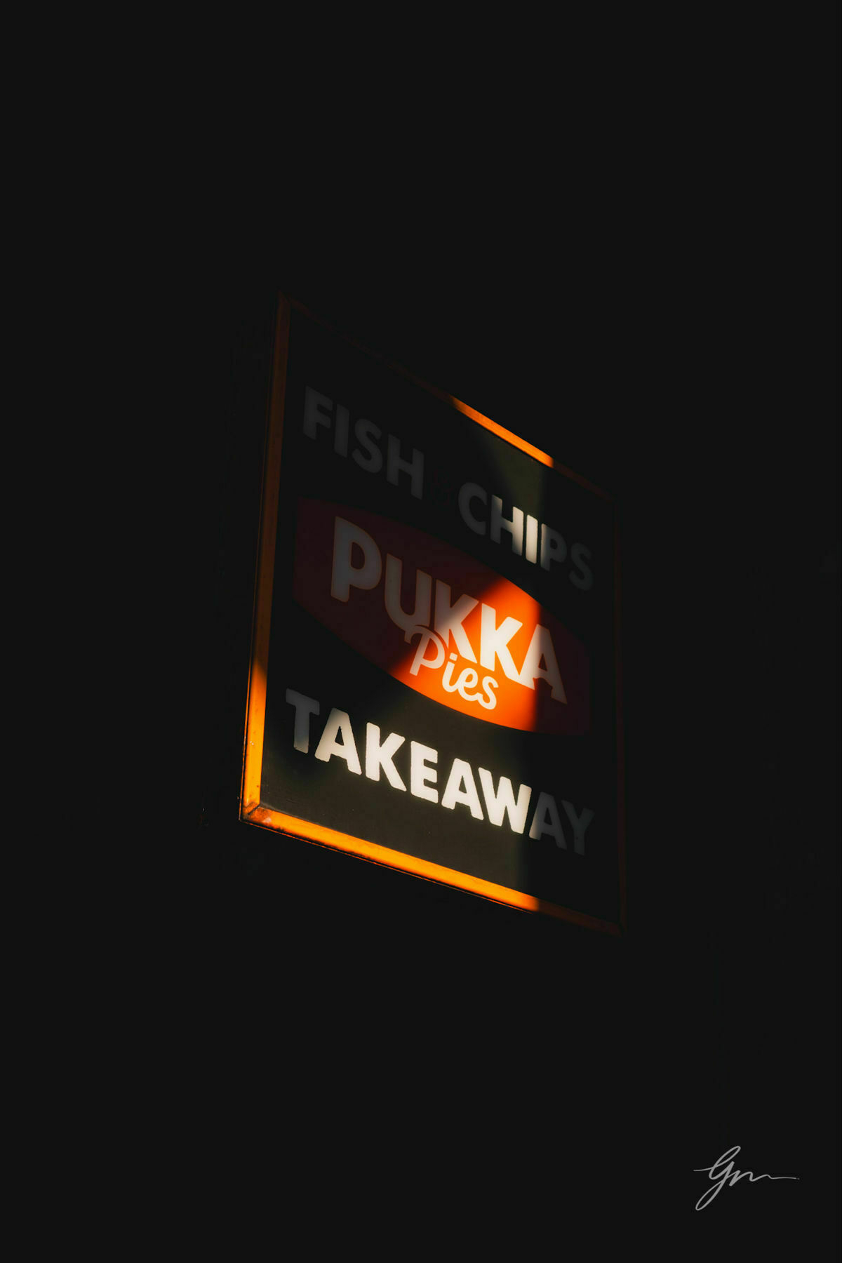 Illuminated signboard in the dark advertising "Fish  Chips" and "Pukka Pies Takeaway".