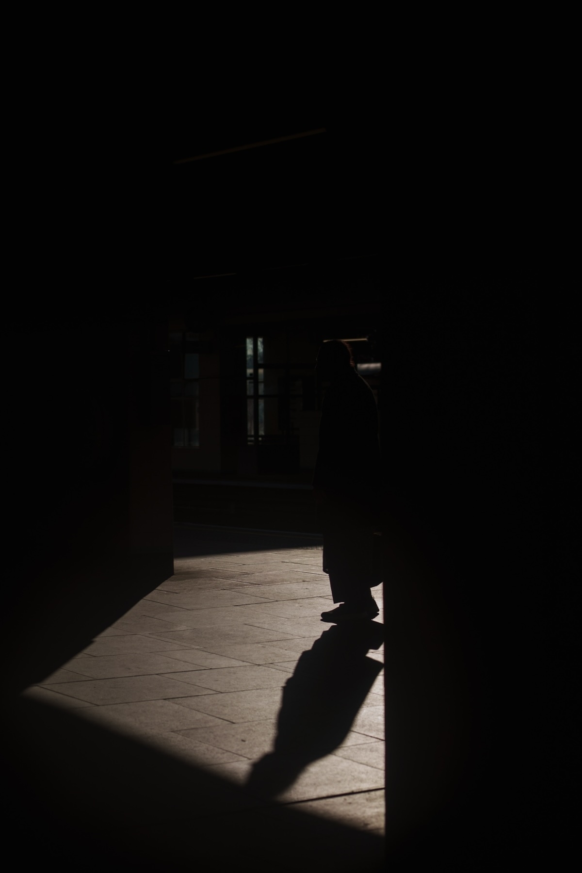 Silhouette of a person standing in a dimly lit area, casting a long shadow on the floor.