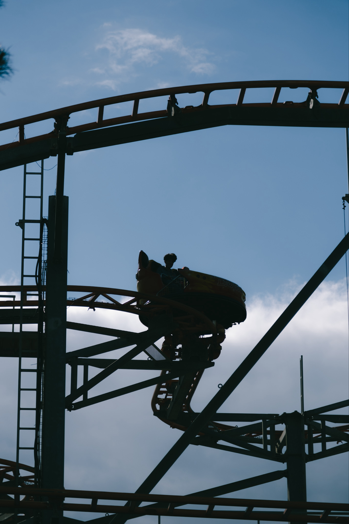 A silhouetted roller coaster car with riders is captured against a blue sky with some clouds.