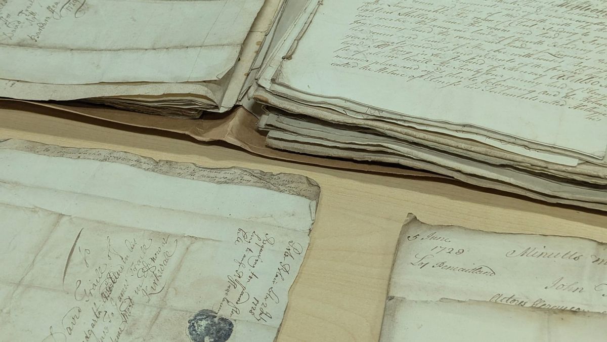 A close up photo of archival documents from the 1720s. A thick folder lies open and two pages are out for inspection