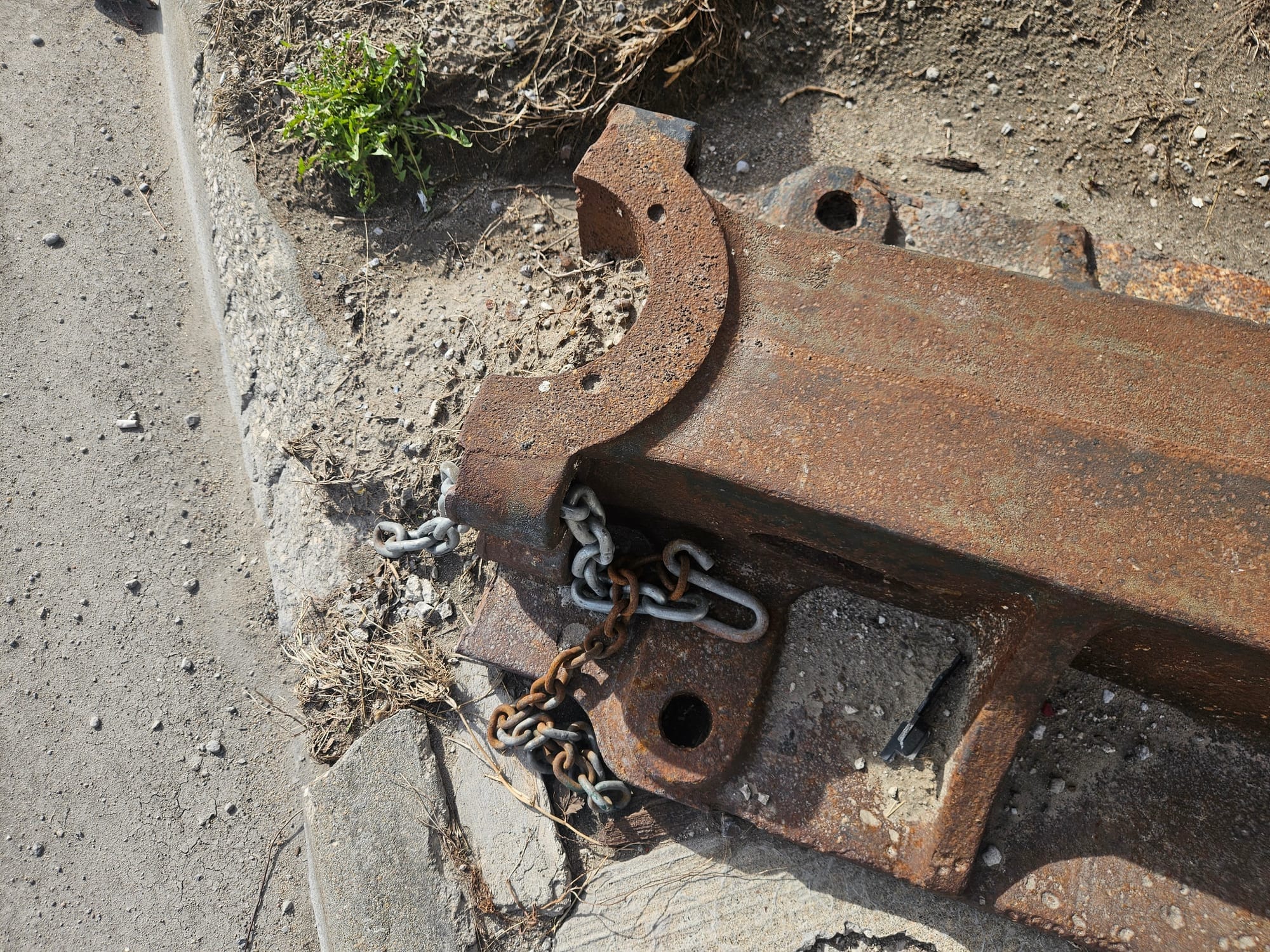 A semicircular flange at the end of the metal object, very rusty, with a chain running through the hole at the bottom.