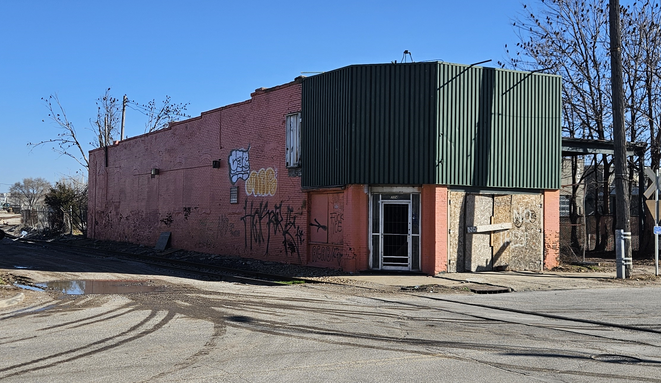 A dilapidated building with "No Trespassing" spraypainted on cheap plywood across the front. Various graffiti is visible all along the side of the building. The front door has no panes.