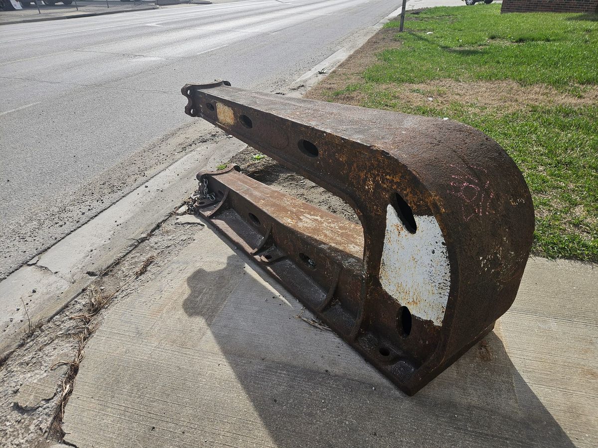 A large, cast iron object, vaguely U-shaped, with several holes throughout. It is rusty, pocked, and scattered with graffiti.
