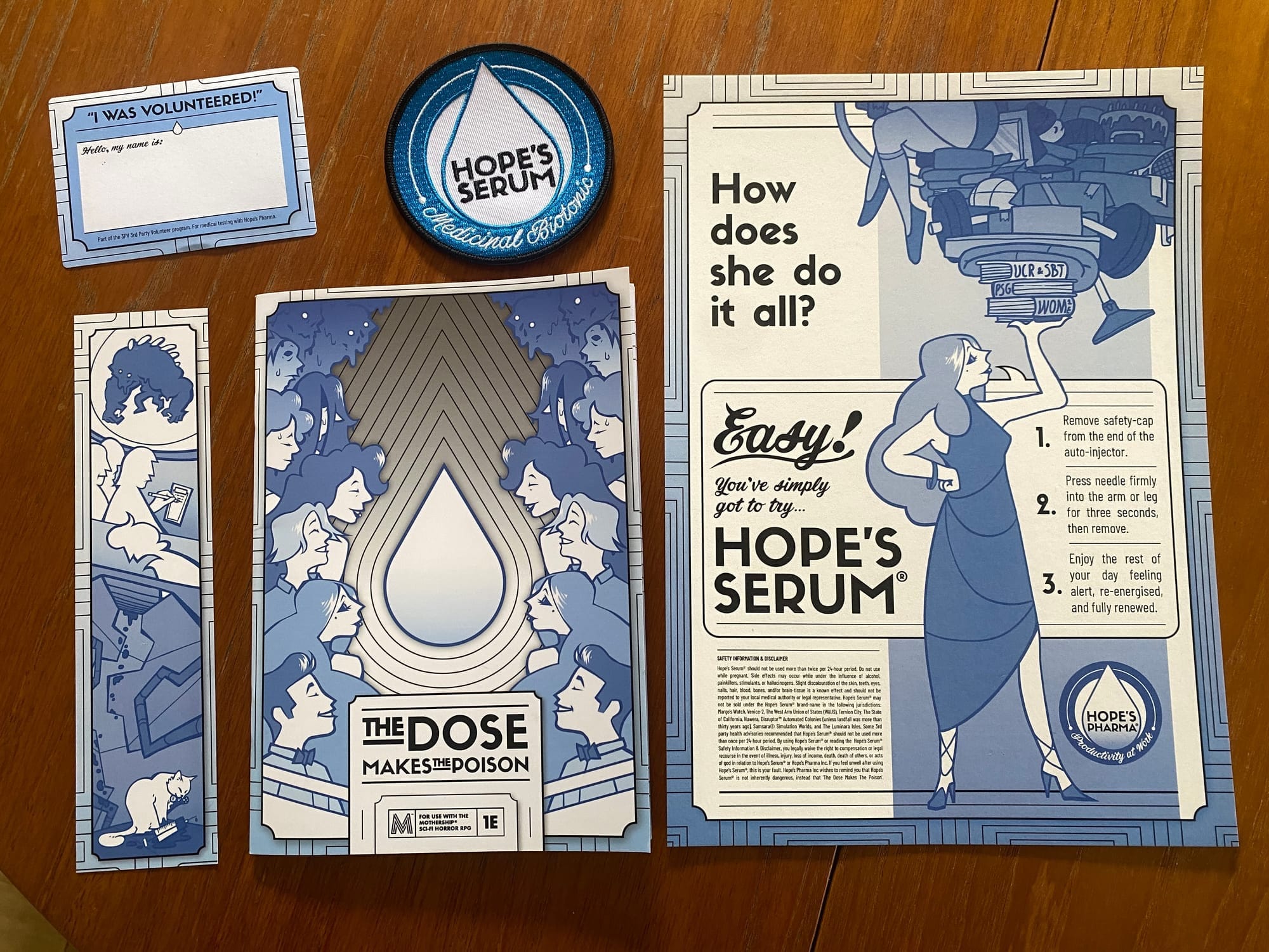 An A5 zine, embroidered patch, poster, bookmark, and sticker arranged neatly on a dark wooden table.