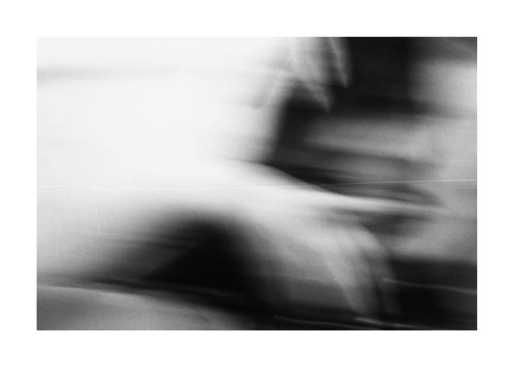 A black and white image of a blurred womans face (right frame) with her hands around her head, a finger across her lips