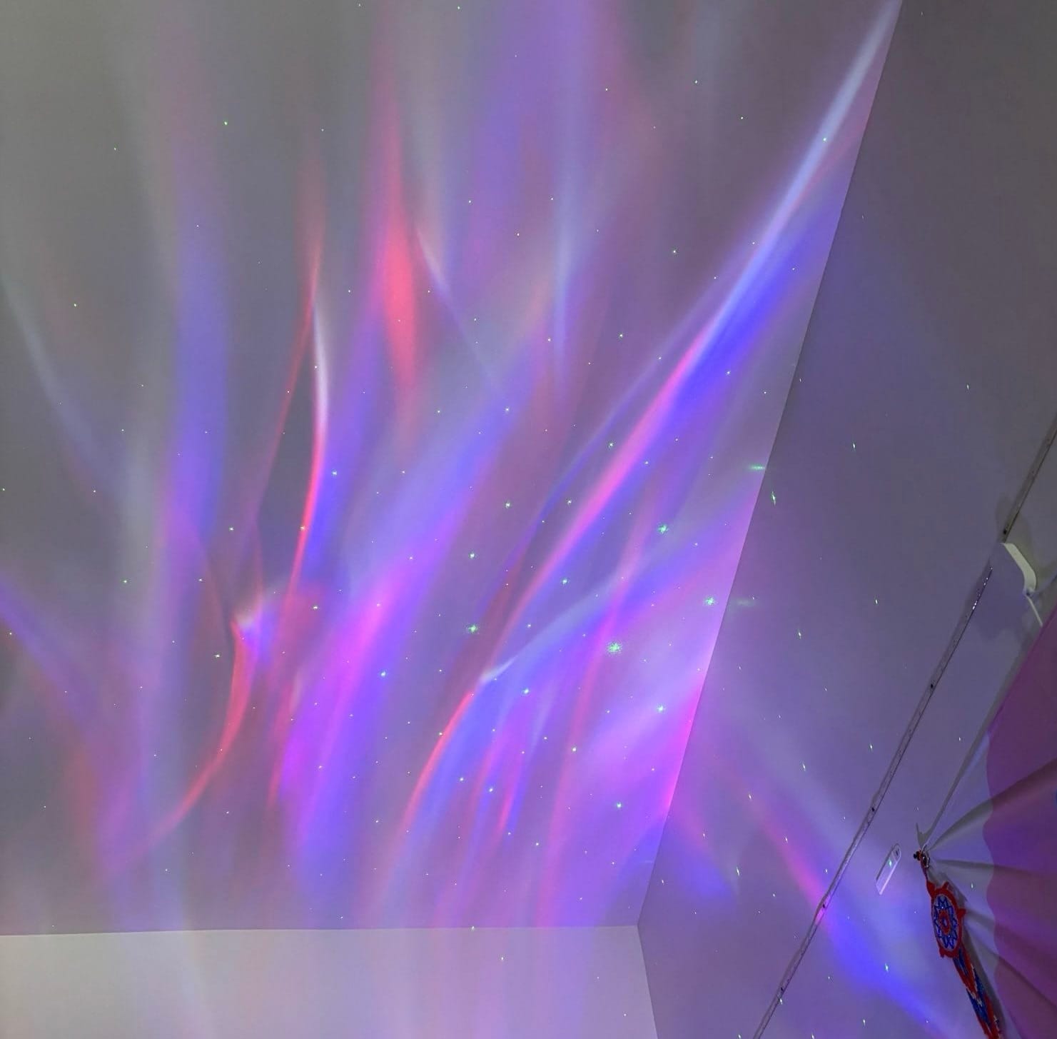 Lights projected on the ceiling of an apartment- red and white waves with green stars.