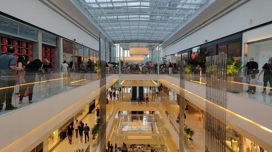 Foto de pátio interno central de um grande shopping center, rodeado de lojas e cheio de pessoas caminhando por ele