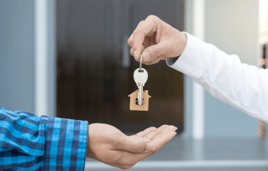 Um mão entregando uma chave com chaveiro de casa para outra mão, representando proprietário e inquilino.