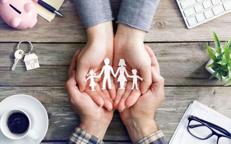 Mãos unidas segurando recortes de papel que representam uma família.