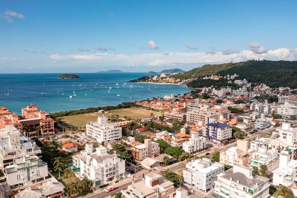 Vista aérea mostrando o bairro Jurerê Internacional, Florianópolis. Se vê praia, as casas e o bairro arborizado e organizado.