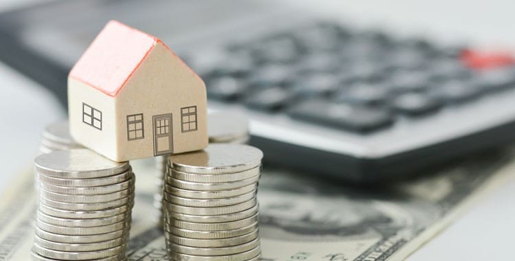Maquete de casa em cima de duas pilhas de moedas.