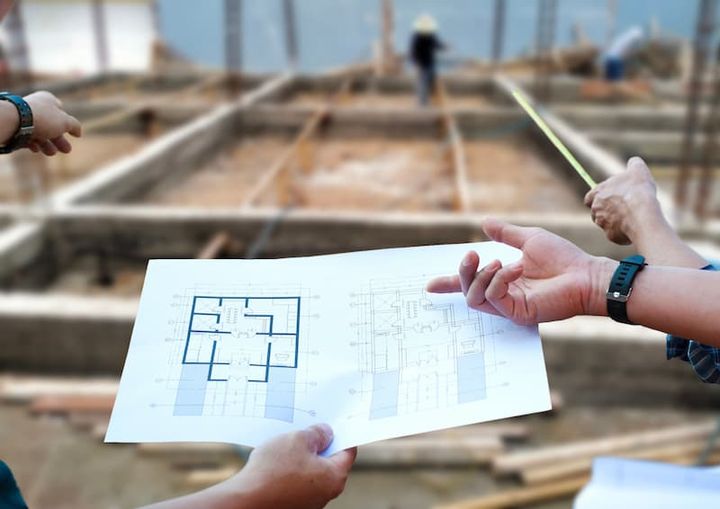 Arquiteto conferindo canteiro de obra com planta do projeto impresso em mãos.