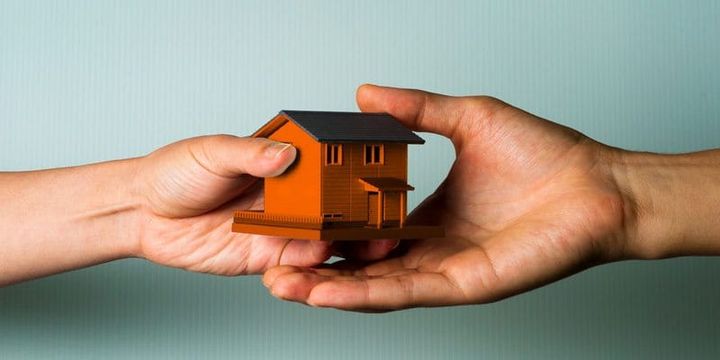 Uma mão passando a maquete de uma casa para outra mão.