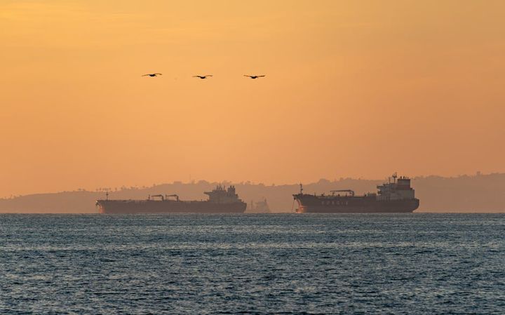 Silhouetted oil tankers at sunset on the Pacific Ocean near Long Beach, California — crude oil supply chain.