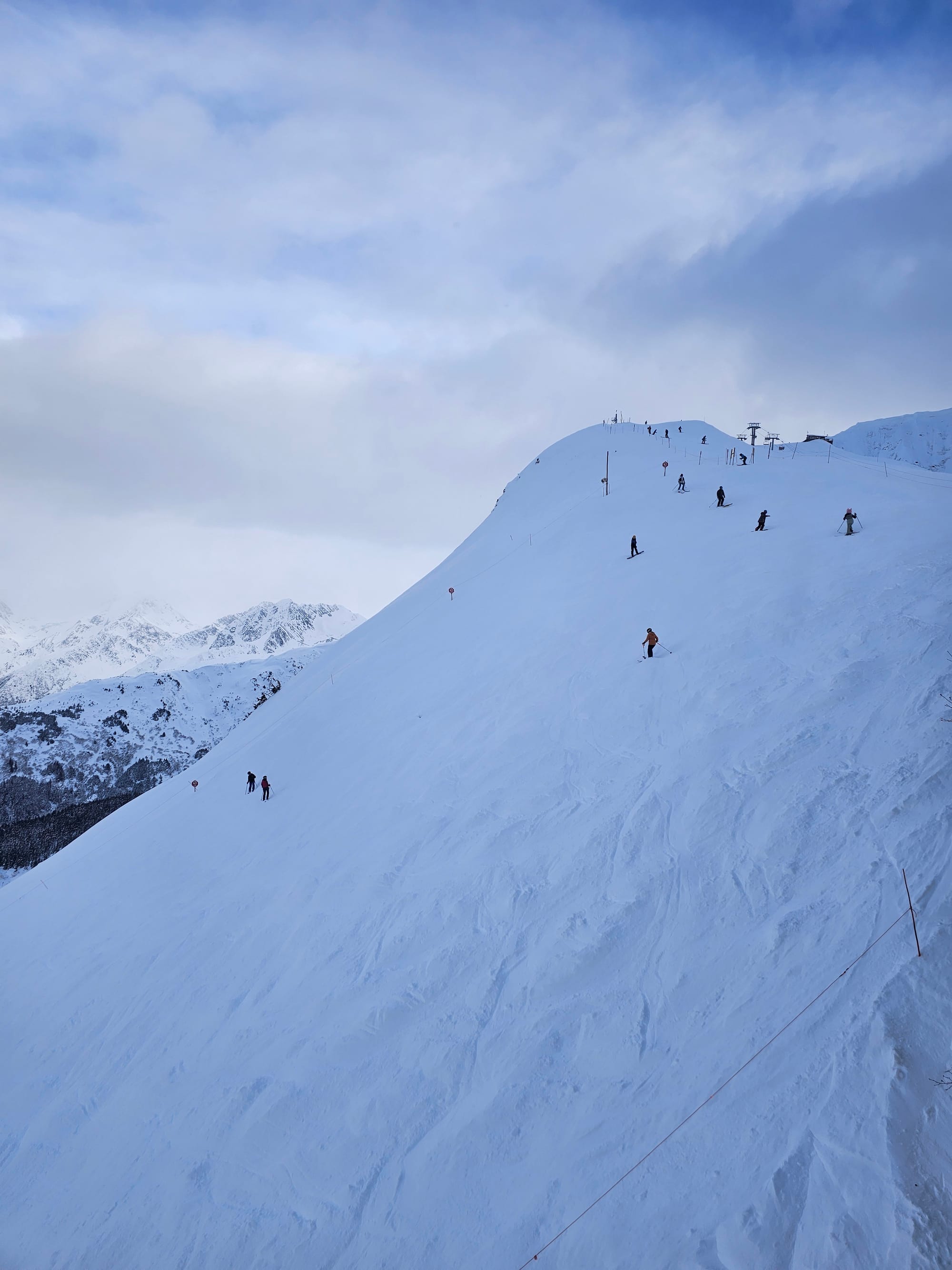 Skiers descending Mt. Alyeska — small figures against a vast white face, the Chugach Mountains stretching beyond in every direction.