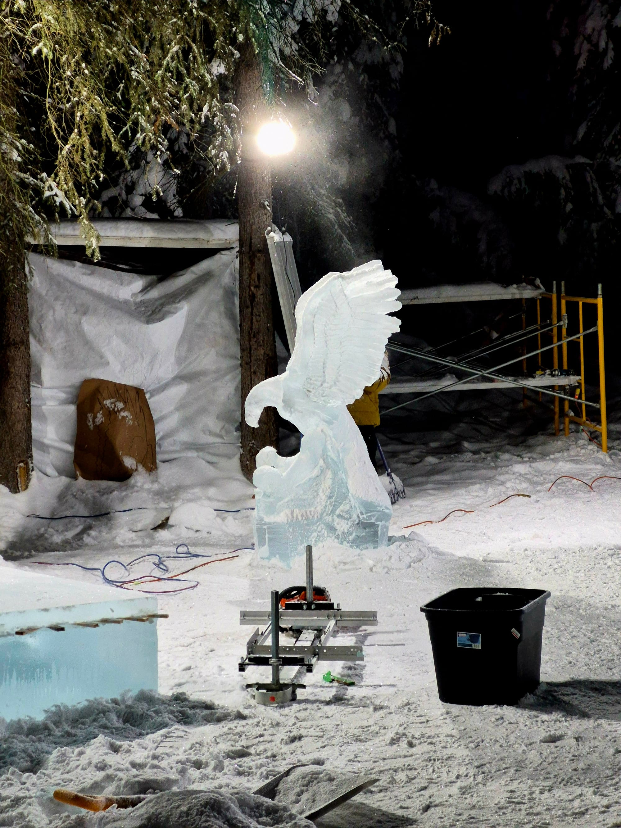 An eagle taking shape in ice at the World Ice Art Championships — precision carving underway under floodlights in subzero Fairbanks.