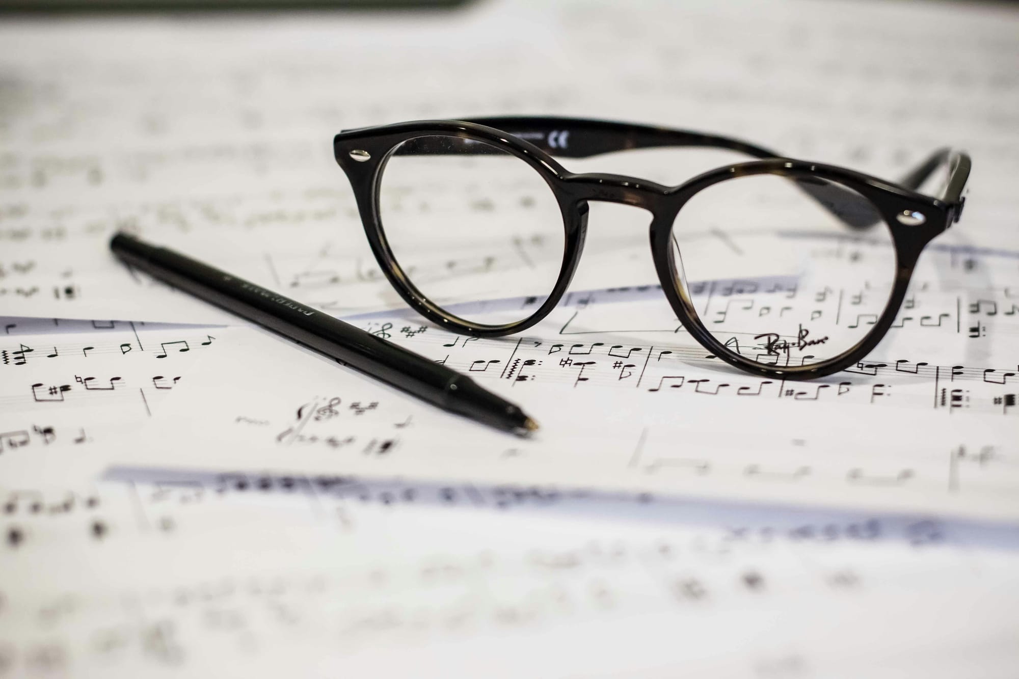 Scattered pages of sheet music with a black pen and glasses sitting on top.