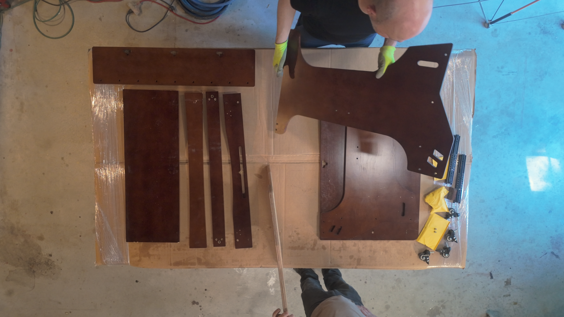 A top down view of a table with parts of a desk on it. A bald white man is holding a large side piece of the desk.