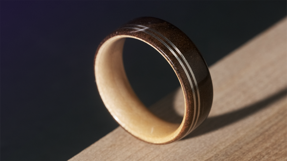 A two-toned wooden ring with two thing metal inlays sitting on top of soli piece of wood