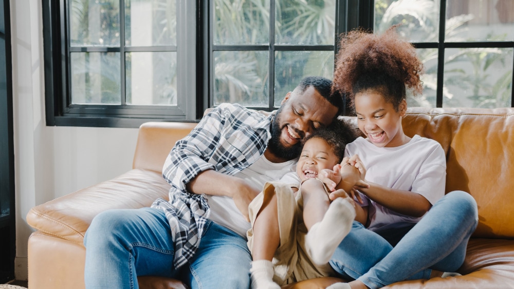 Happy cheerful african american family dad and daughter having fun cuddle play on sofa while birthday at house.