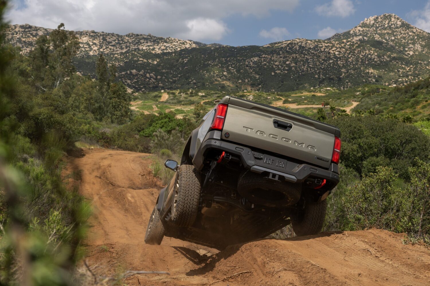 Tacoma Trailhunter lifts a rear wheel on a dirt trail, demonstrating suspension articulation.