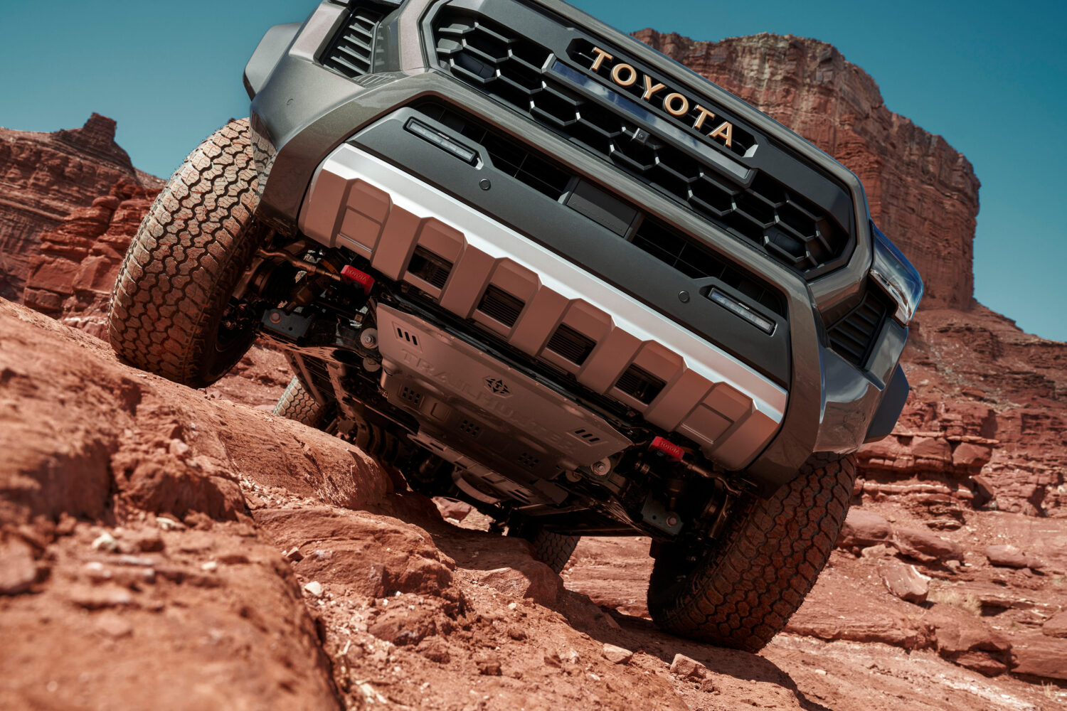 2025 Toyota Tacoma Trailhunter climbs red rock terrain, showing front skid plate and grille.