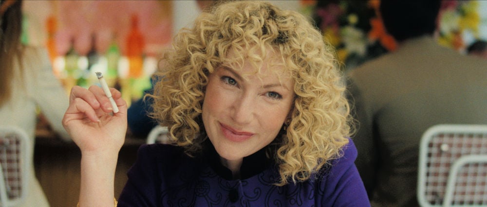 A character in Monsters_ The Lyle and Erik Menendez Story smiles while holding a cigarette, highlighting a moment of complexity within the drama. cast of monsters