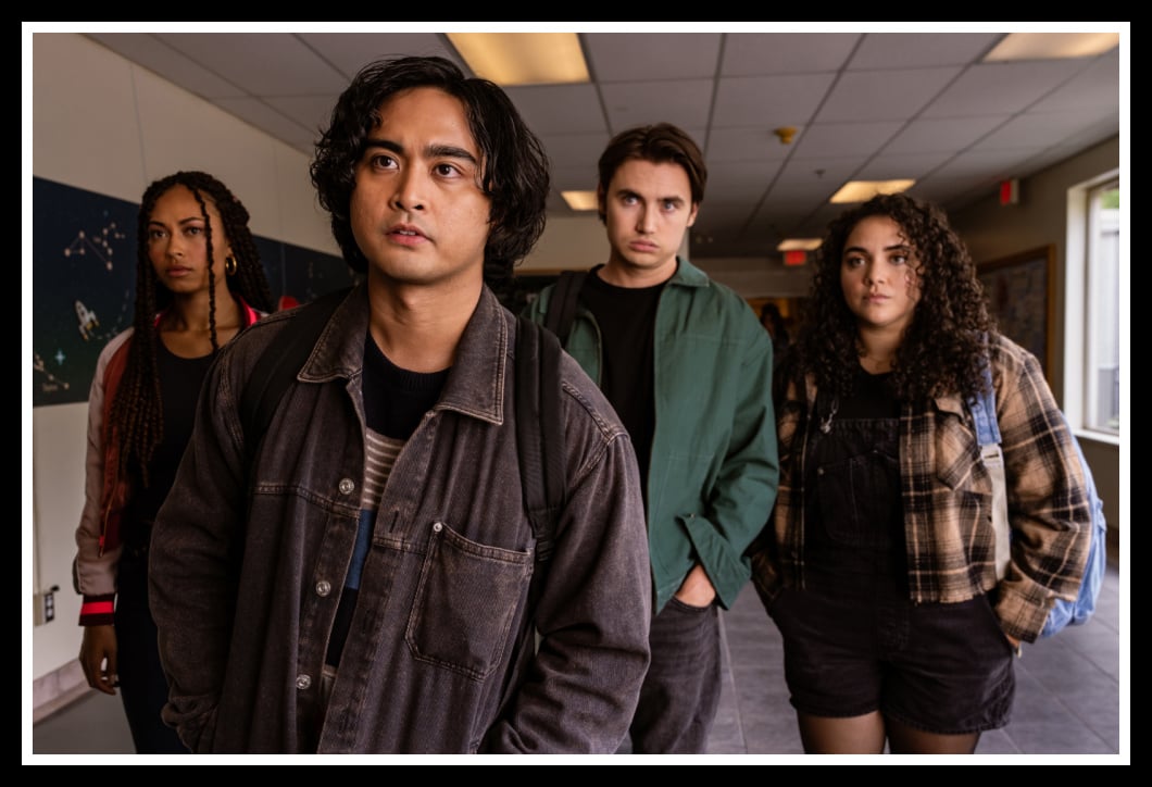 A group of students, including Simon Elroy (Kristian Ventura) and Nicole Herrera (Kiara Pichardo), stand tensely in a school hallway in School Spirits Season 2.