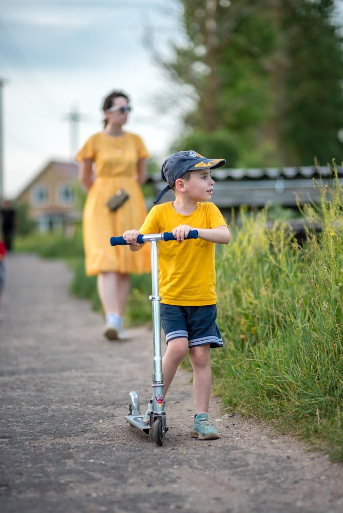 A woman and a boy are riding a scooter with a woman in a yellow dress
