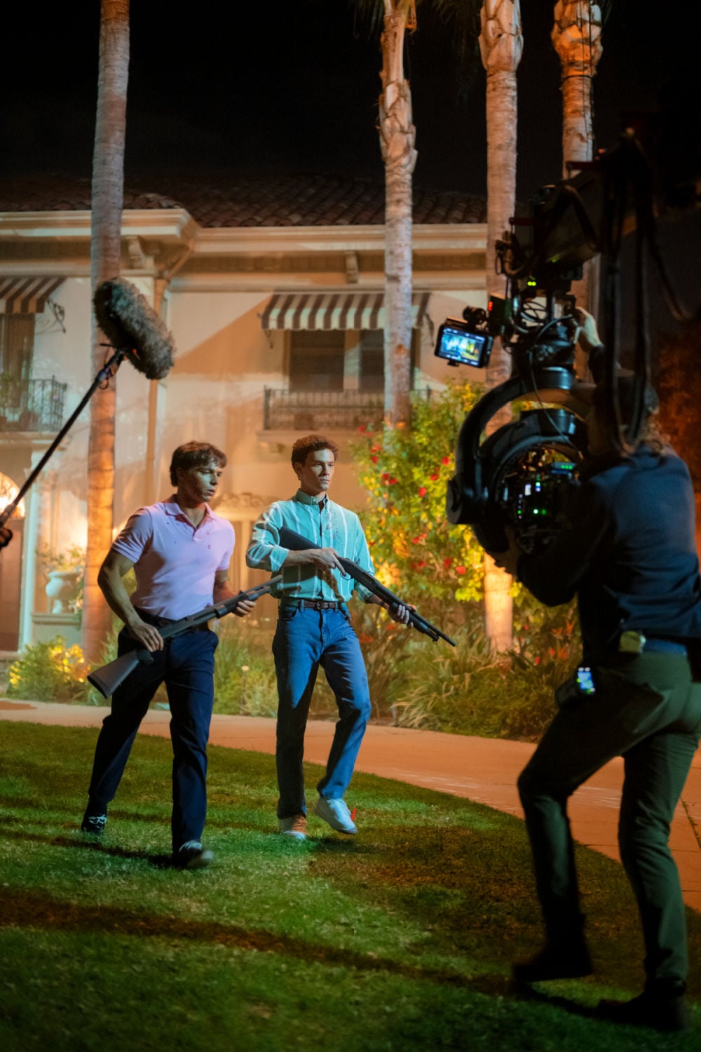 Behind-the-scenes image from 
 Cast of Monsters The Lyle and Erik Menendez Story, showing two characters with rifles, along with the film crew, illustrating the intensity of the production.