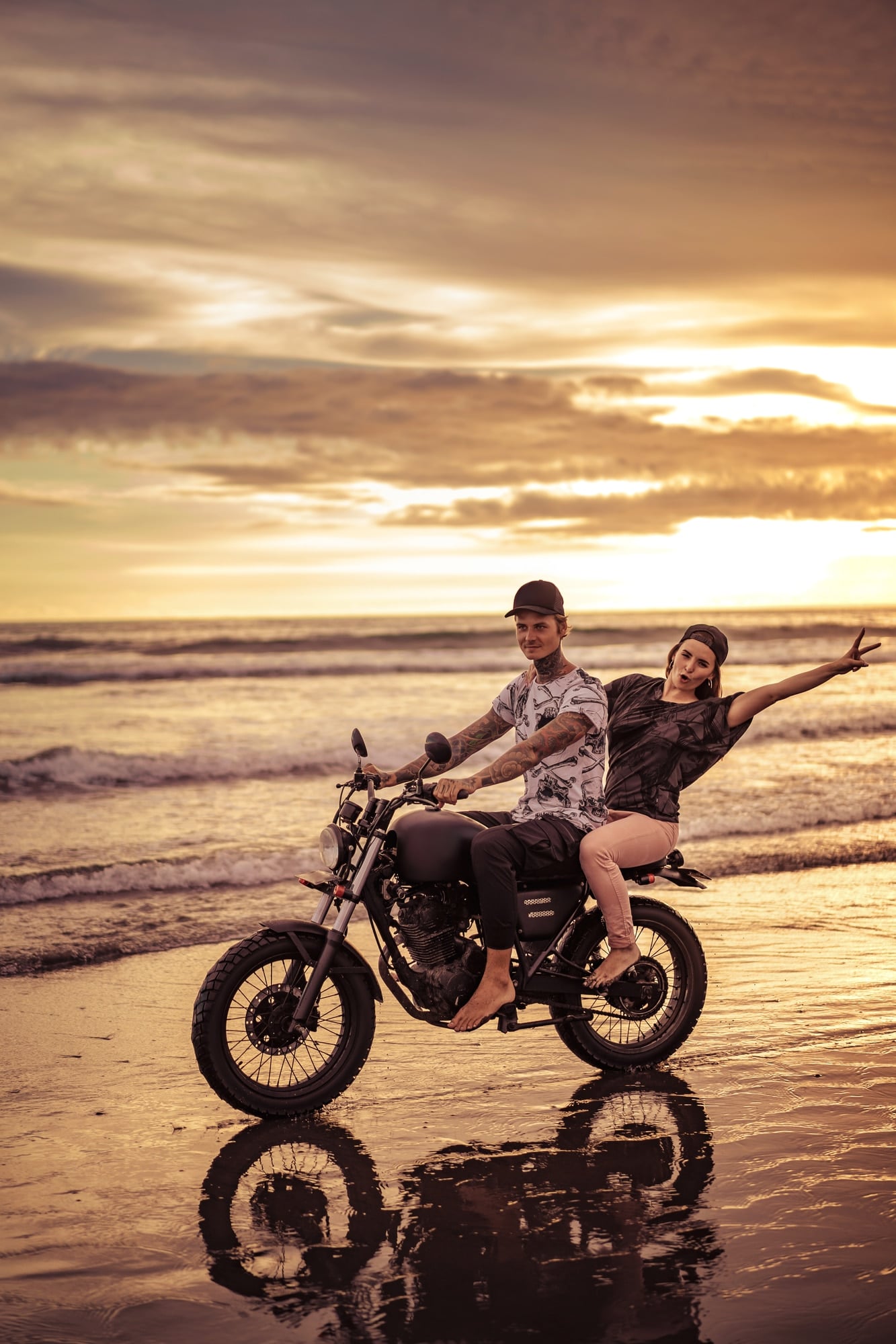 Young male and female riding a motorcycle on the beach sunset