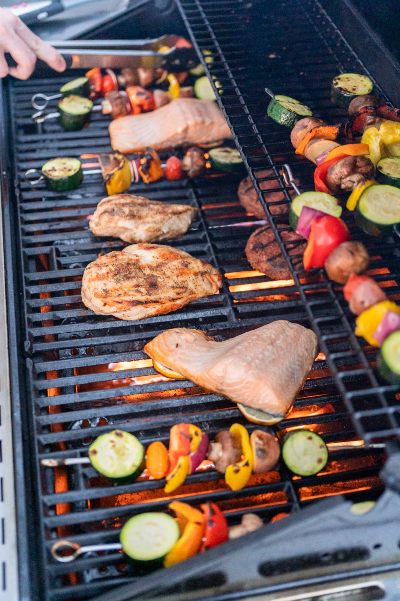 Grilling an Atlantic salmon, chicken breast, vegetable skewers, and vegetarian burgers on an outdoor grill.