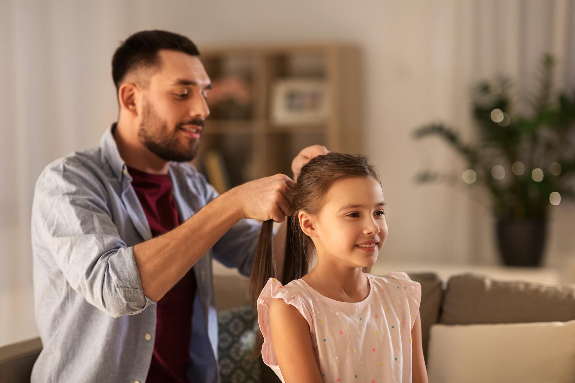 Dad braids his daughter’s hair on the couch—an everyday “Girl Dad” moment at home.