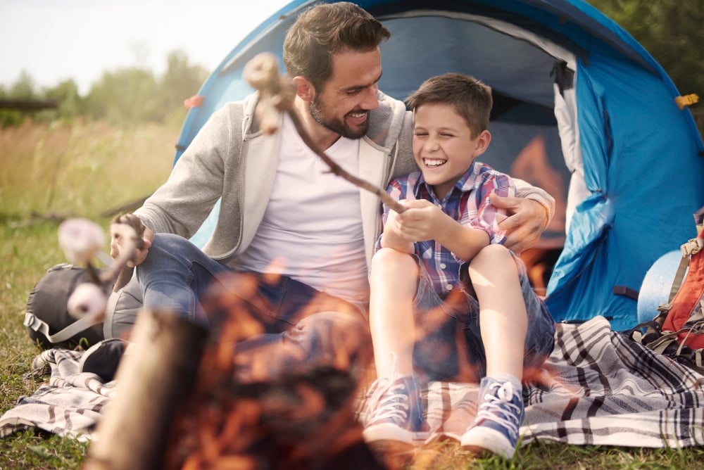Father and son sitting next a camp fire, roasting marshmallows. 