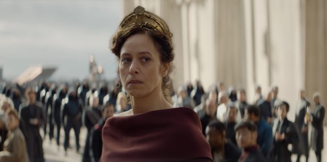 Jodhi May portrays Sister Irina, a high-ranking figure in the Bene Gesserit. The grand setting and her solemn expression hint at a scene of political intrigue.