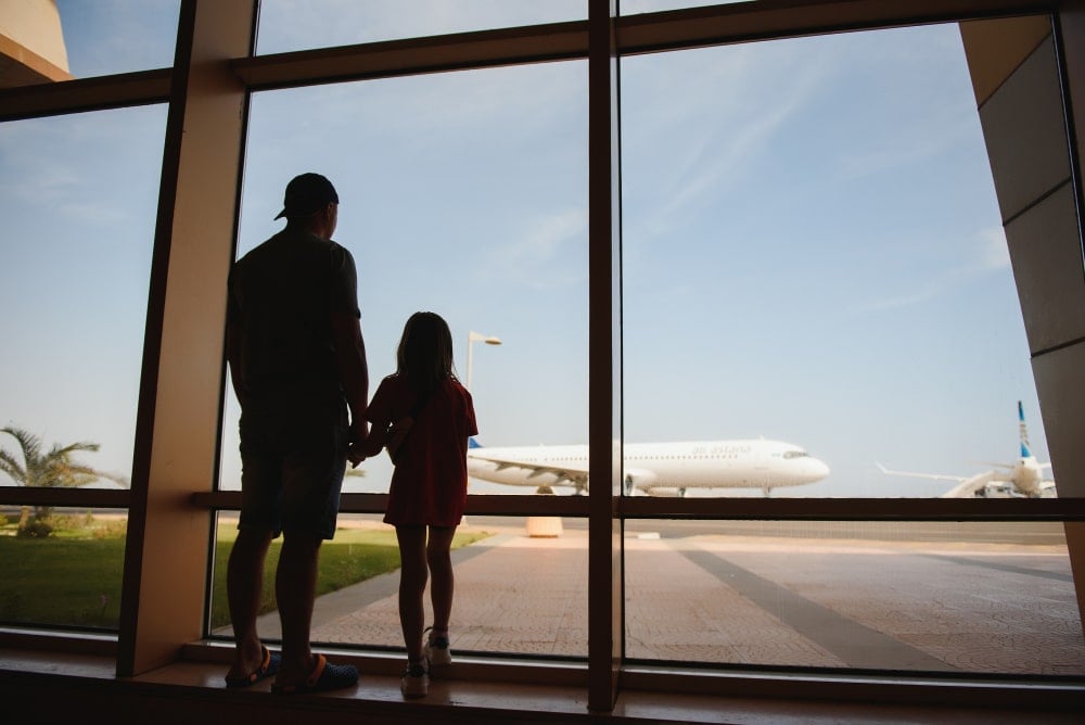 Father and daughter looking out an airport window,
